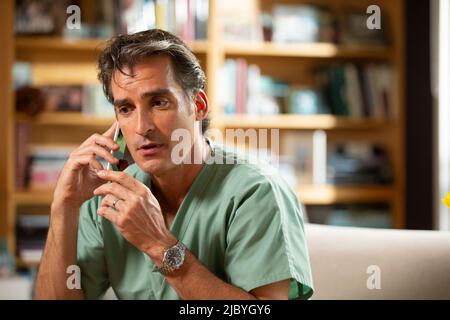 Hispanischer Arzt, der in seinem Büro Telemedizin praktiziert und mit dem Patienten am Handy spricht Stockfoto