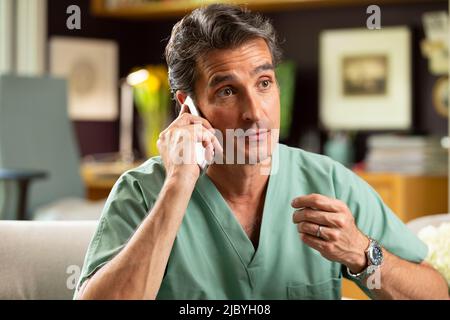 Hispanischer Arzt, der in seinem Büro Telemedizin praktiziert und mit dem Patienten am Handy spricht Stockfoto