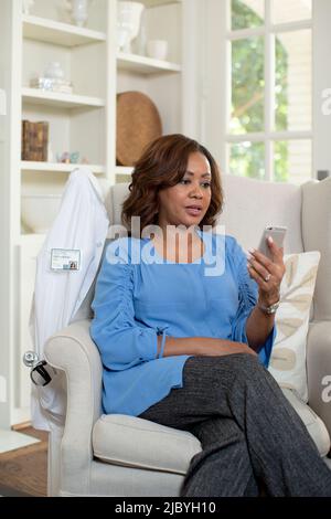 Eine schwarze Ärztin mittleren Alters zu Hause, die Telemedizin leistet und mit einem Mobiltelefon mit dem Patienten während eines Videoanrufs spricht Stockfoto