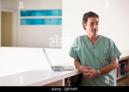 Porträt eines hispanischen männlichen Arztes in seinem Haus, der eine Pause vom Praktizieren der Telemedizin macht und von der Kamera schaut Stockfoto