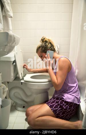 Die junge Frau auf dem Boden in ihrem Badezimmer fühlte sich neben der Toilette krank und sprach mit dem Arzt am Handy Stockfoto