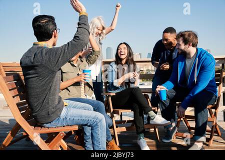 Eine Gruppe junger Mitarbeiter, die sich auf der Dachterrasse aufmachen, einen Drink zu sich nehmen und Erfolge feiern, erreichte sie per Handy Stockfoto