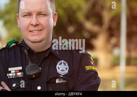 Porträt eines Polizisten, der draußen mit gekreuzten Armen steht und lächelnd auf die Kamera blickt Stockfoto