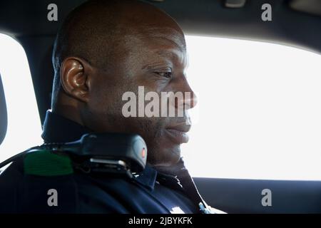 Nahaufnahme Porträt eines uniformierten Polizeibeamten, der im Kaderwagen sitzt und auf den Computer im Auto blickt Stockfoto