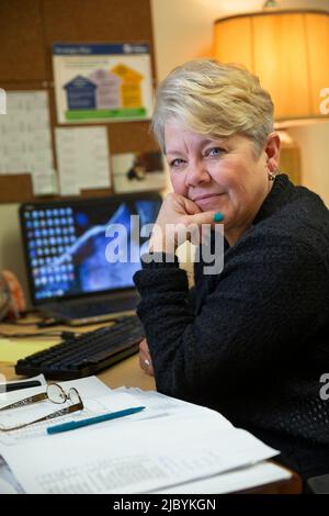 Porträt einer Frau, die an ihrem Schreibtisch im Bürogebäude sitzt und den Kopf in der Hand hält, eine Pause von der Arbeit macht und die Kamera anschaut Stockfoto