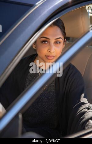 Porträt einer Frau, die auf dem Fahrersitz des Autos mit geöffneter Tür sitzt und die Kamera anschaut Stockfoto