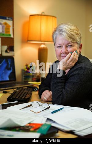 Porträt einer Frau, die an ihrem Schreibtisch im Bürogebäude sitzt und den Kopf in der Hand hält, eine Pause von der Arbeit macht und die Kamera anschaut Stockfoto