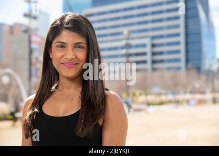 Lächelndes Porträt einer jungen ethnischen Frau, die in einem schwarzen Tank-Top im Park steht Stockfoto