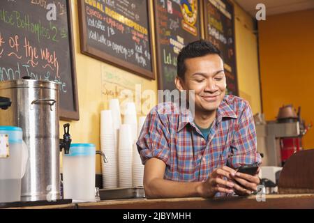 Malaysische Unternehmer hinter Café Zähler mit Handy Stockfoto