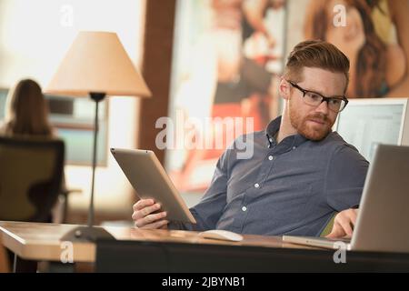 Kaukasische Geschäftsmann mit digitalen Tablet und Laptop im Büro Stockfoto