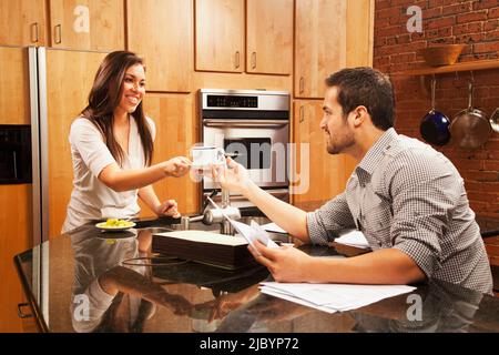 Hispanische Frau, die ihrem Mann Kaffee in der Küche gab Stockfoto