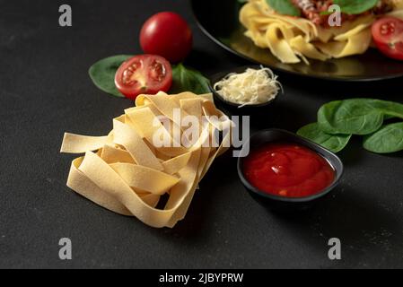 Rohe Pasta auf dunklem Hintergrund mit Zutaten zum Kochen Stockfoto