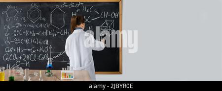 Studentin, die mit Kreide auf einer Tafel schreibt, chemische Formeln auf einer Tafel, Rückansicht. Chemie. Wissenschaft und Bildung. Stockfoto