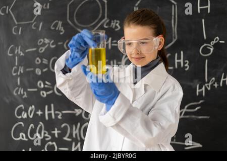 Schülerin im weißen Mantel, die im Chemielabor Experimente mit Flüssigkeit macht, junge Chemikerin mit Kolben Stockfoto