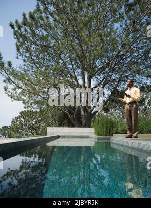 Afrikanische amerikanische Mann SMS auf Handy Swimming Pool Stockfoto