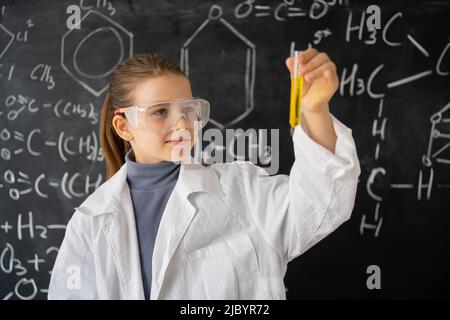 Bildungskonzept. Kleine Kinder Wissenschaftler schauen sich einen Erlenmeyerkolben an, der Chemikalien enthält, um Experimente im Labor durchzuführen, Schülerin Stockfoto