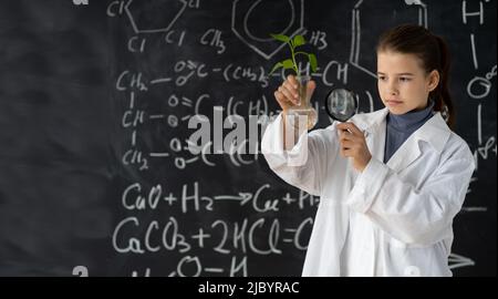 Junges Mädchen studiert kleine Pflanze in der Grundschule Wissenschaft Klasse. Student hält Lupe. Earth Day Holiday-Konzept. Weltumwelttag Stockfoto