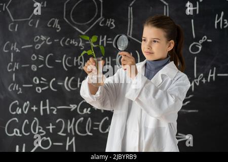 Junges Mädchen studiert kleine Pflanze in der Grundschule Wissenschaft Klasse. Student hält Lupe. Earth Day Holiday-Konzept. Weltumwelttag Stockfoto