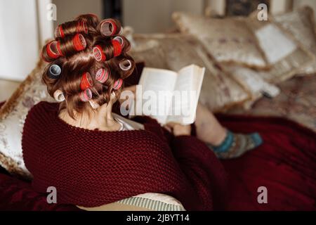 Alte aktive ältere Frau mit Rollen im Haar kümmern sich an ihrem freien Tag um sich selbst. Entspannen und Ausruhen auf dem Bus zu Hause Stockfoto