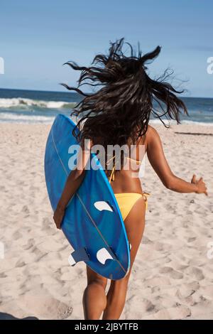 Gemischte Rassen Frau rennt mit Surfbrett am Strand Stockfoto