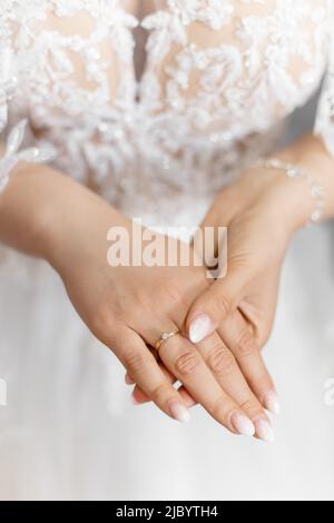 Nahaufnahme Foto von eleganten, glänzenden sanften Frau Hände halten einander, Braut mit ausgezeichneter Maniküre. Weißes Hochzeitskleid Stockfoto