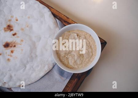 Flaches Lay von berühmten frisch gebackenen Pita Brot und tauchen Hummus in weiße Schüssel in Holzschale auf den Tisch. Selektiver Fokus. Stockfoto