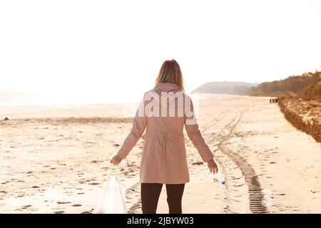 Rückansicht einer Freiwilligen, die am Strand steht und Flasche, Reinigungsbereich und Meer vor Plastikmüll hält. Speicherplatz kopieren Stockfoto