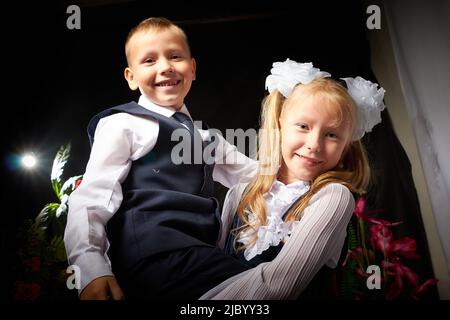 Mädchen und Jungen, die Grundschüler in Uniform mit Spaß auf schwarzem Hintergrund mit Blumen ist. Bruder und Schwester am 1. September in Russland Stockfoto