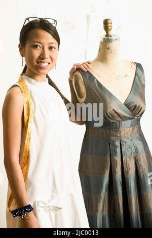 Asiatische weibliche Mode-Designer neben Kleid Puppe Stockfoto