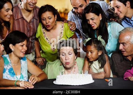 Ältere Frau Ausblasen der Kerzen auf ihrem Geburtstagskuchen Stockfoto