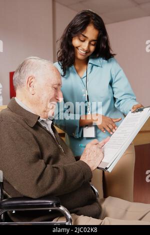 Krankenschwester hält ein Formular für einen älteren Mann zu unterzeichnen Stockfoto