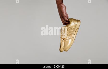 Detailaufnahme von Blackmans Hand mit goldlackierten Sneakers vor dem weißen Brett. Stockfoto