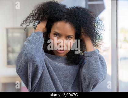 Eine Frau mittleren Alters läuft mit ihren Händen durch die Haare und schaut auf die Kamera. Stockfoto