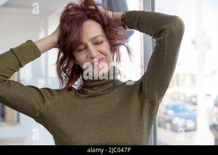 Frau mittleren Alters mit reichlich Energie läuft ihre Hände lächelnd durch ihr Haar. Stockfoto