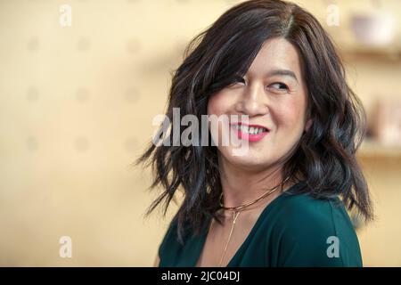 Nahaufnahme eines Porträts einer Frau mittleren Alters mit schwarzem Haar, das lächelnd über ihre Schulter schaut. Stockfoto