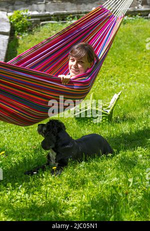 Frau entspannt sich in einer Hängematte und ihr Hund liegt unten in der Schweiz. Stockfoto