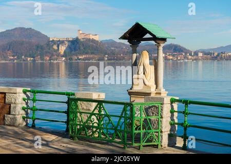 Gehweg mit Statue und Schloss Rocca Borromea di Angera am Lago Maggiore in Angera, Lombardei, Italien. Stockfoto