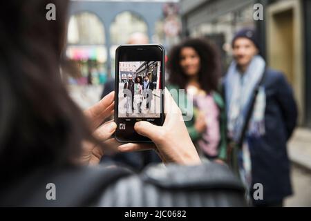Frau auf den Straßen von London, die Freunde mit dem Mobiltelefon fotografiert Stockfoto