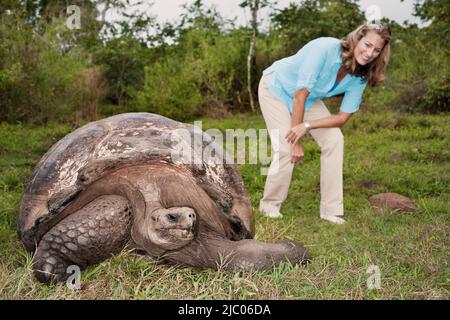 Ecuador, Galapagos-Inseln, Frau, die im Gras in der Nähe der Riesenschildkröte steht Stockfoto