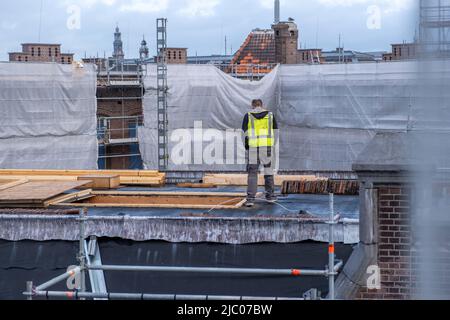 Dämmarbeiten an der Dachkonstruktion des Gebäudes. Arbeiter mit gelber Weste auf dem Dach, Metallgerüst. Amsterdam, Niederlande Stockfoto