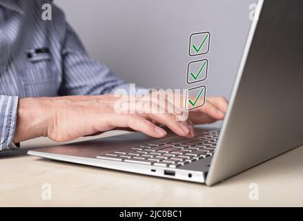 Mann, der am Laptop arbeitet und erreichte Ziele mit Ticks markiert oder an einer Umfrage teilnimmt und richtige Antworten notiert. Checkliste, Planung, Zeitmanagement-Konzept. Männliche Hände an der Computertastatur. Hochwertige Fotos Stockfoto