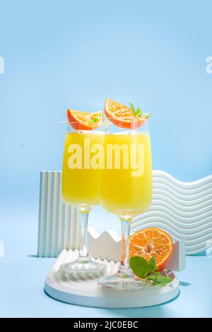 Klassischer Sommer-Mimosas-Cocktail mit Orangensaft auf hellblauem Hintergrund. Sommerliches Bar-Menü mit Kopierbereich Stockfoto