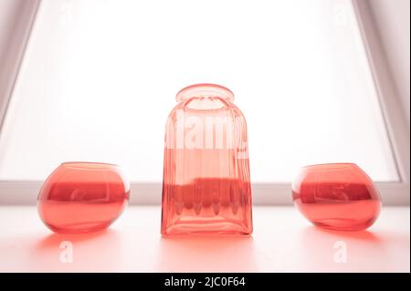 Drei leere rote Glasvasen auf der Fensterbank. Stockfoto