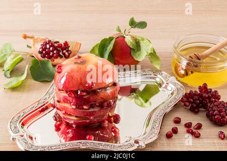 Ein reifer großer Apfel mit Honig und Granatapfelkernen auf einem silbernen Tablett. Ein traditioneller Leckerbissen für den Feiertag der Juden von Roshashana. Vorderansicht Stockfoto