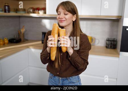 Hübsche junge Frau schnüffelt ein frisches französisches Baguette Stockfoto