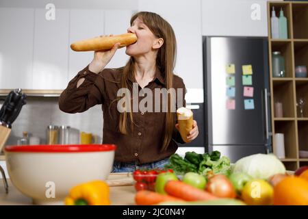 Hungrige Frau, die beim Kochen in der Küche ein Baguette isst Stockfoto