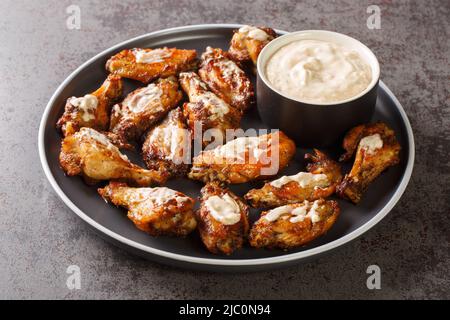 Eine Portion gegrillter Hähnchenflügel mit weißer Alabama-Grillsoße in Nahaufnahme auf einem Teller auf dem Tisch. Horizontal Stockfoto