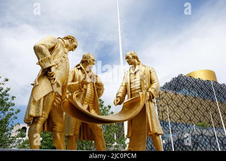 Diese vergoldete Bronzestatue, bekannt als die ‘Golden Boys’, befindet sich vor der New Birmingham Library und dem ICC in der Broad Street, Birmingham. Die Statue wurde 2022 nach der Renovierung des hundertjährigen Platzes an diesen neuen Ort verlegt. Die Statue ehrt Matthew Boulton, James Watt und William Murdoch. Sie werden gezeigt, wie sie die Pläne der Dampflokomotive untersuchen. Zusammen revolutionierten diese drei die Dampfmaschine – die Technologie, die buchstäblich die industrielle Revolution vorantreiben würde. Stockfoto