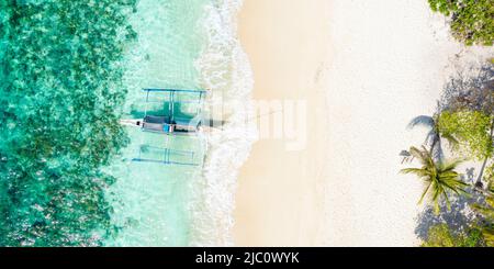 Blick von oben, atemberaubende Luftaufnahme eines Bangka-Bootes vor einem weißen Sandstrand, der von einem türkisfarbenen Wasser umspült wird. Stockfoto
