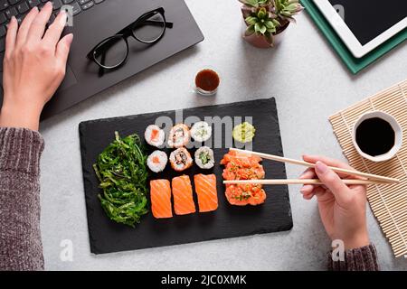 Frau aß Sushi zum Mitnehmen am Schreibtisch über dem Zimmer. Essen von Sushi für die Mittagspause, Mittagessen bei der Arbeit Stockfoto